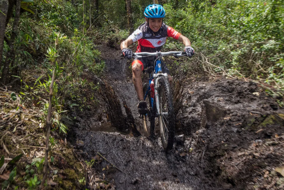 Ciclista de montaña bajando por una rodada de barro profunda en un sendero de bosque