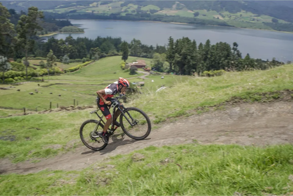 Ciclista de ONE fuera del sillín, con el tronco adelantado sobre el manubrio, acelerando en un tramo de tierra