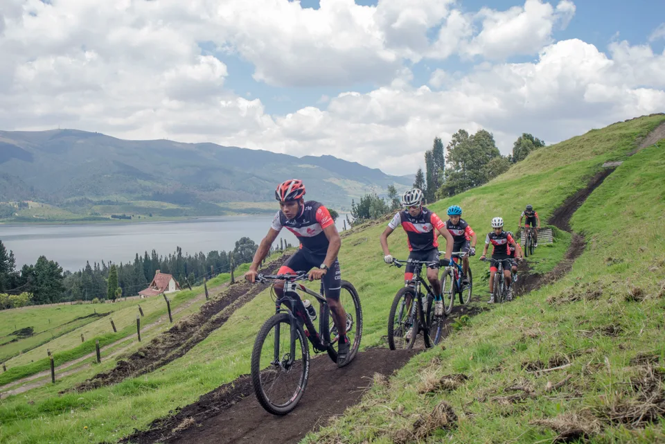 Grupo de ciclistas de montaña subiendo un sendero de tierra junto al embalse