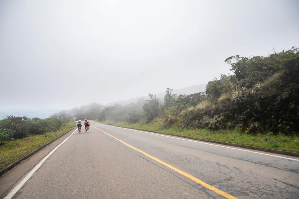 Carretera de montaña entre la niebla con ciclistas al fondo