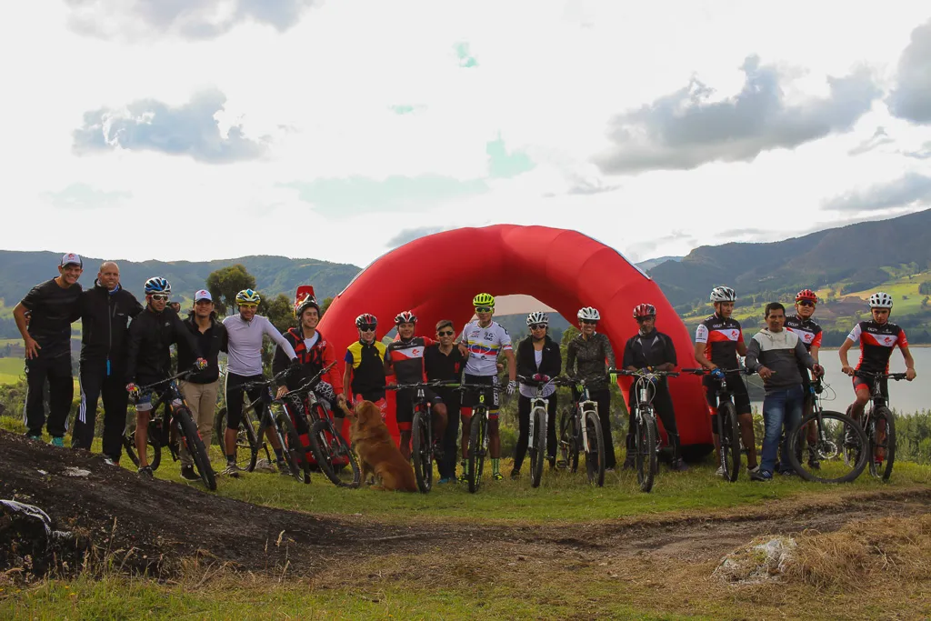 Grupo de ciclistas de montaña de ONE reunidos frente a un arco inflable rojo junto al embalse