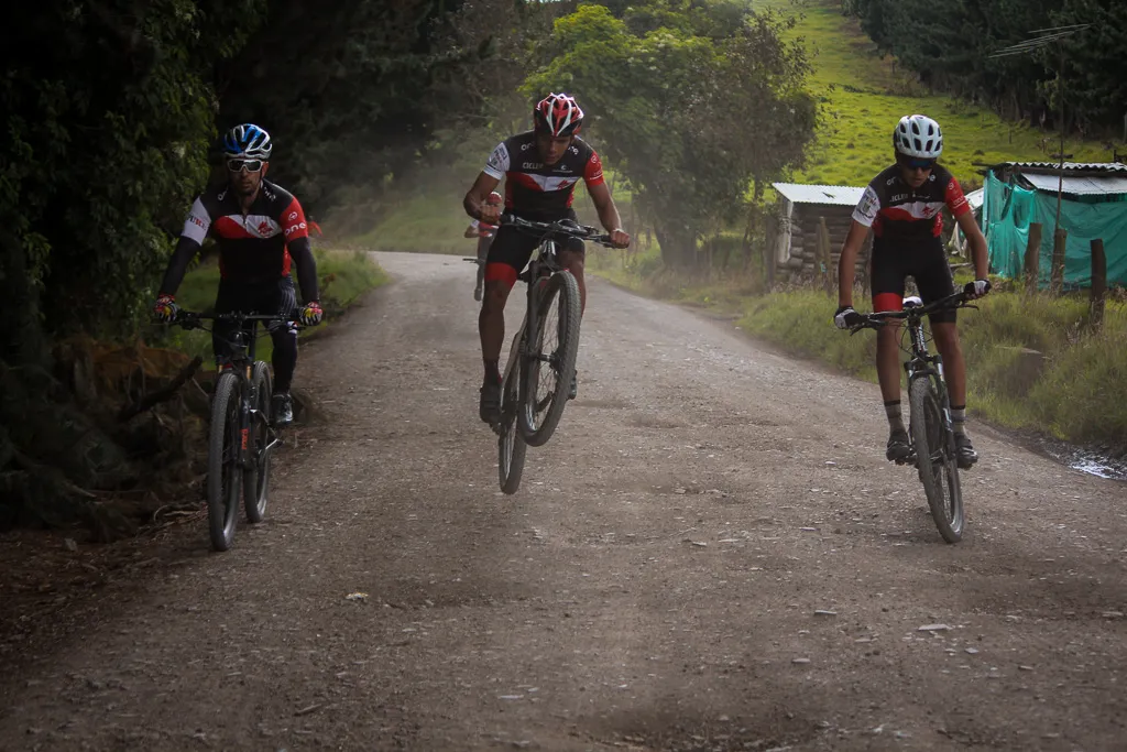 Tres ciclistas de ONE rodando en fila por un camino destapado levantando polvo