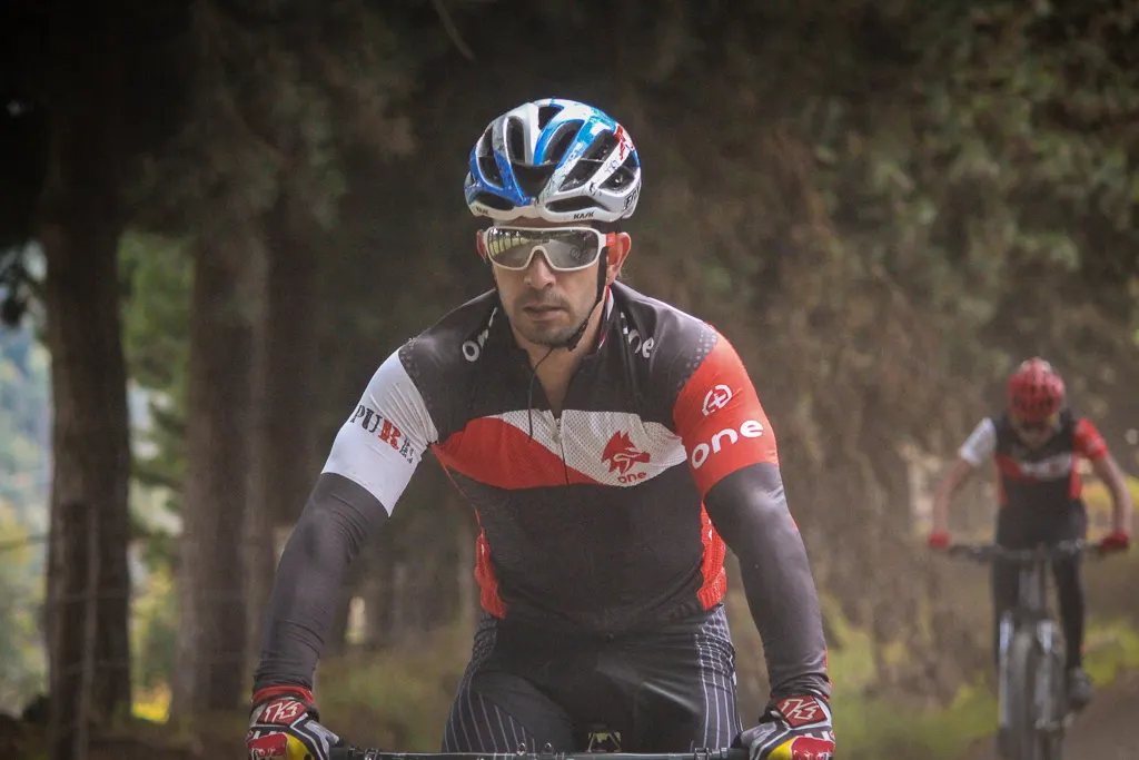 Ciclista de ONE rodando por un camino de tierra entre árboles, con otro ciclista del equipo detrás