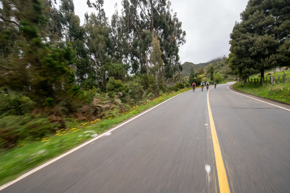 Carretera de montaña con ciclistas de ONE rodando al fondo