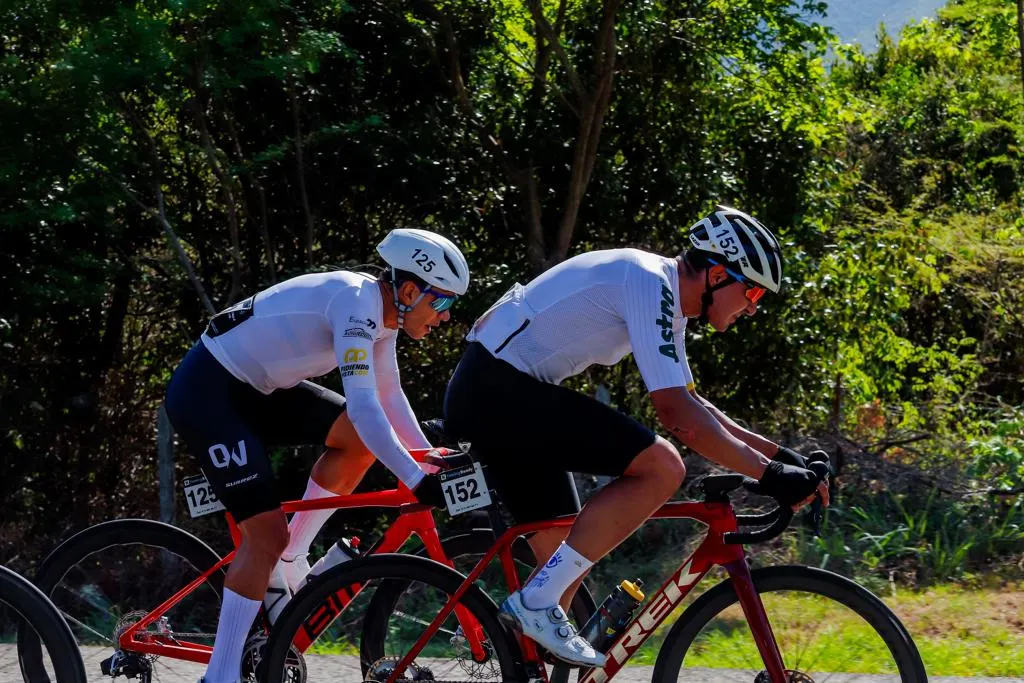 Dos ciclistas con dorsal rodando a rueda en una carrera de ruta